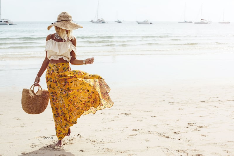 Woman walking on beach in flowing skirt and large hat