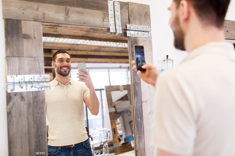 Man smiling as he takes a picture of himself in a mirror