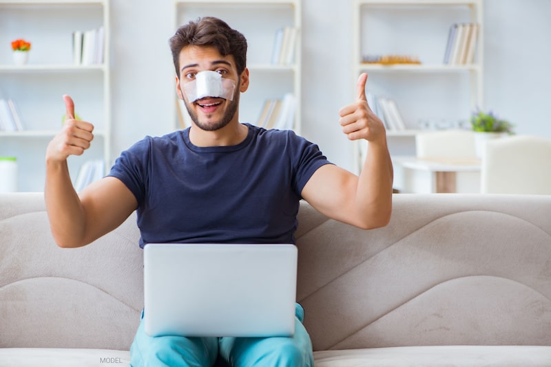 Man sitting on the couch with bandages on his nose after having a rhinoplasty.