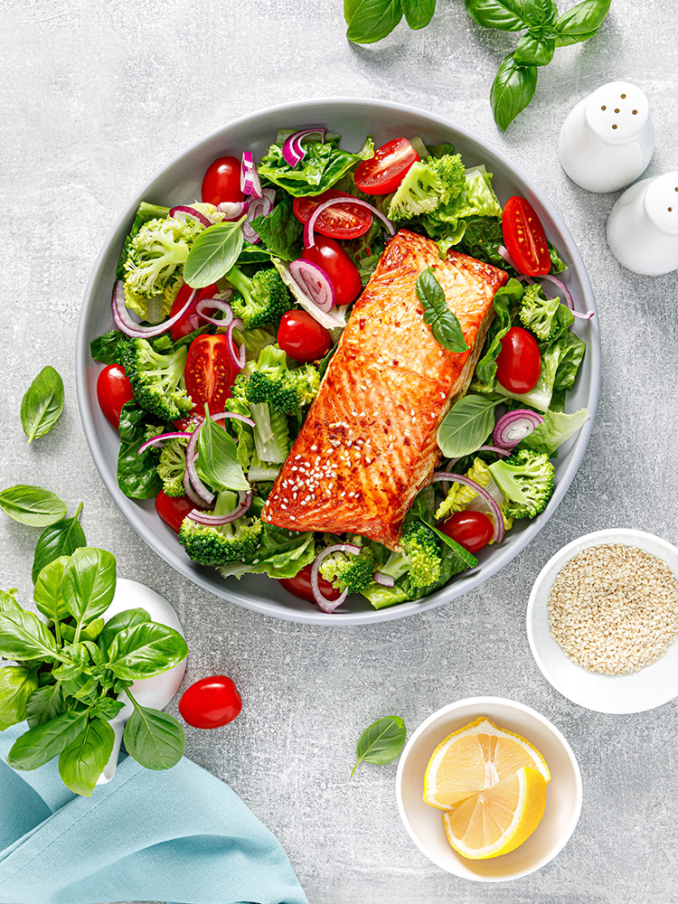 Bright, colorful top-down image of a green salad with grilled salmon and a side of lemons.